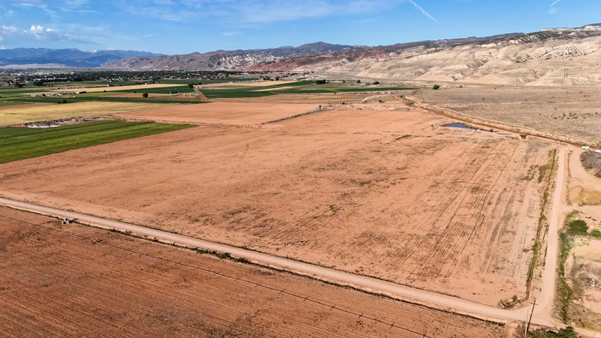 Expansive open land featuring a dirt road, surrounding fields, and distant mountains