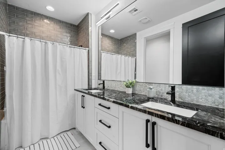 Dual vanity with white cabinetry, black hardware, integrated rectangular sinks, and a dark stone countertop