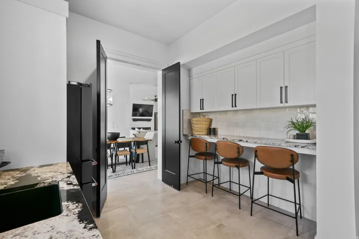 Built-in bar area with stone-finish countertop, white cabinetry, and subway tile backsplash