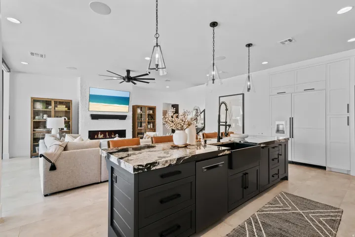 Spacious kitchen island with stone countertop and farmhouse sink, integrated refrigerator and cabinetry, recessed lighting, and a modern linear fireplace