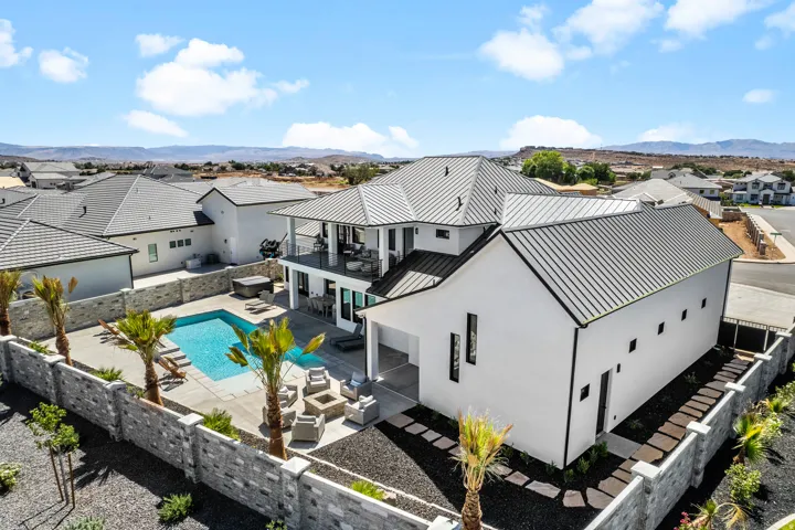 Contemporary white exterior with a dark metal roof, featuring a rectangular swimming pool, an elevated balcony, and a stone-clad perimeter wall