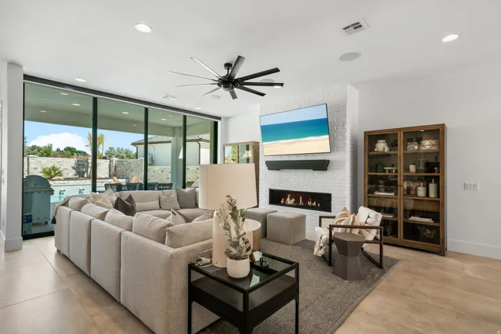 Expansive glass sliding doors, linear fireplace with white brick surround, recessed lighting, and a multi-blade ceiling fan