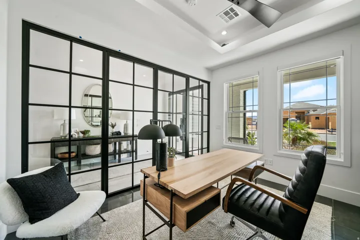 Steel-framed glass partition wall, tray ceiling with recessed lighting, two large windows, dark tile flooring, and a ceiling fan