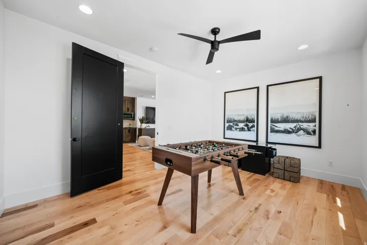 Recreation room showcasing warm wood-finish flooring, recessed ceiling lighting, and a ceiling fan