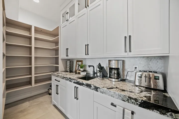 Pantry featuring extensive built-in shelving, white shaker cabinetry with dark hardware, a stone countertop, and a black sink with a dark faucet