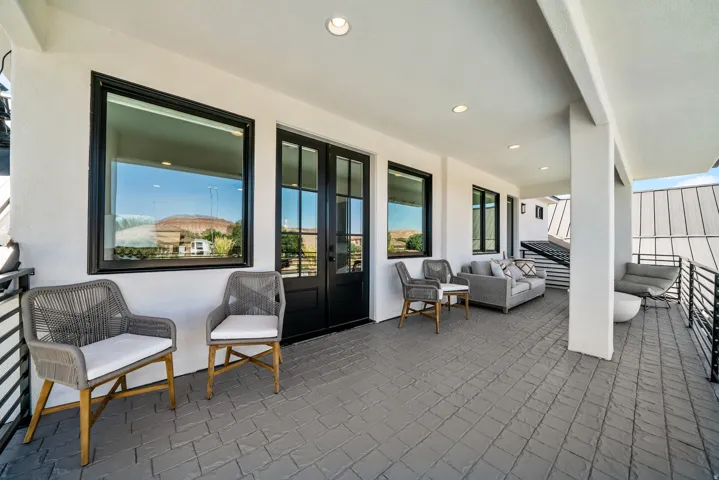 Covered outdoor patio with textured flooring, recessed lighting, black-framed windows, and a black wrought iron railing