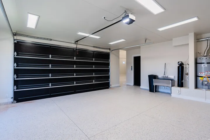 Attached garage with an epoxy floor, black sectional garage door, multiple overhead light fixtures, a utility sink, and a water heater