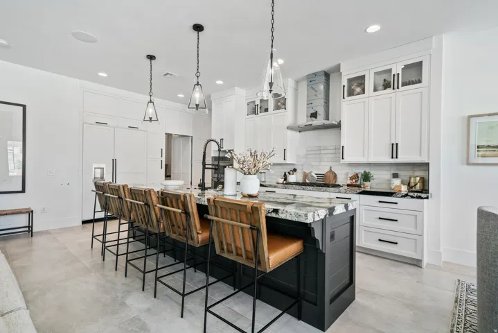 Kitchen with custom cabinetry, a large central island with seating, pendant lighting, built-in appliances, and light-colored flooring