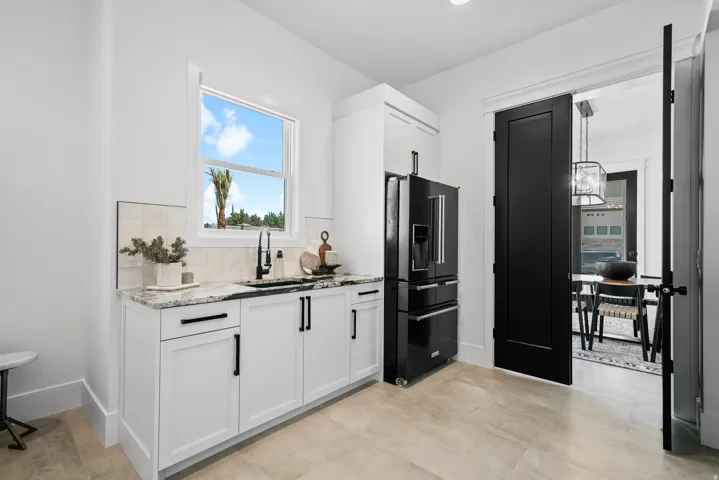 White cabinetry with black hardware, granite countertop, undermount sink with a matte black faucet, and a black refrigerator