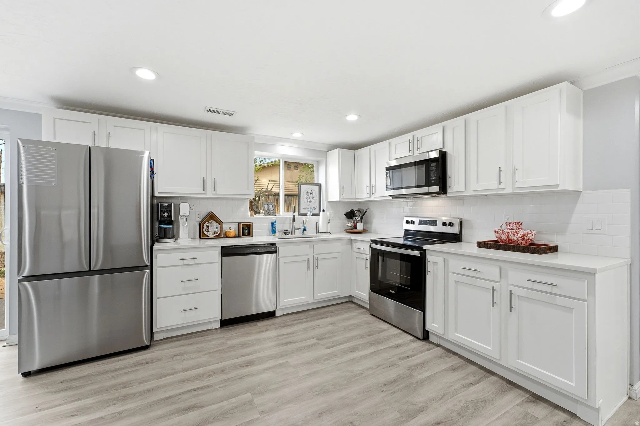 Contemporary kitchen with white cabinetry, stainless steel appliances, light countertops, subway tile backsplash, and wood-finish flooring