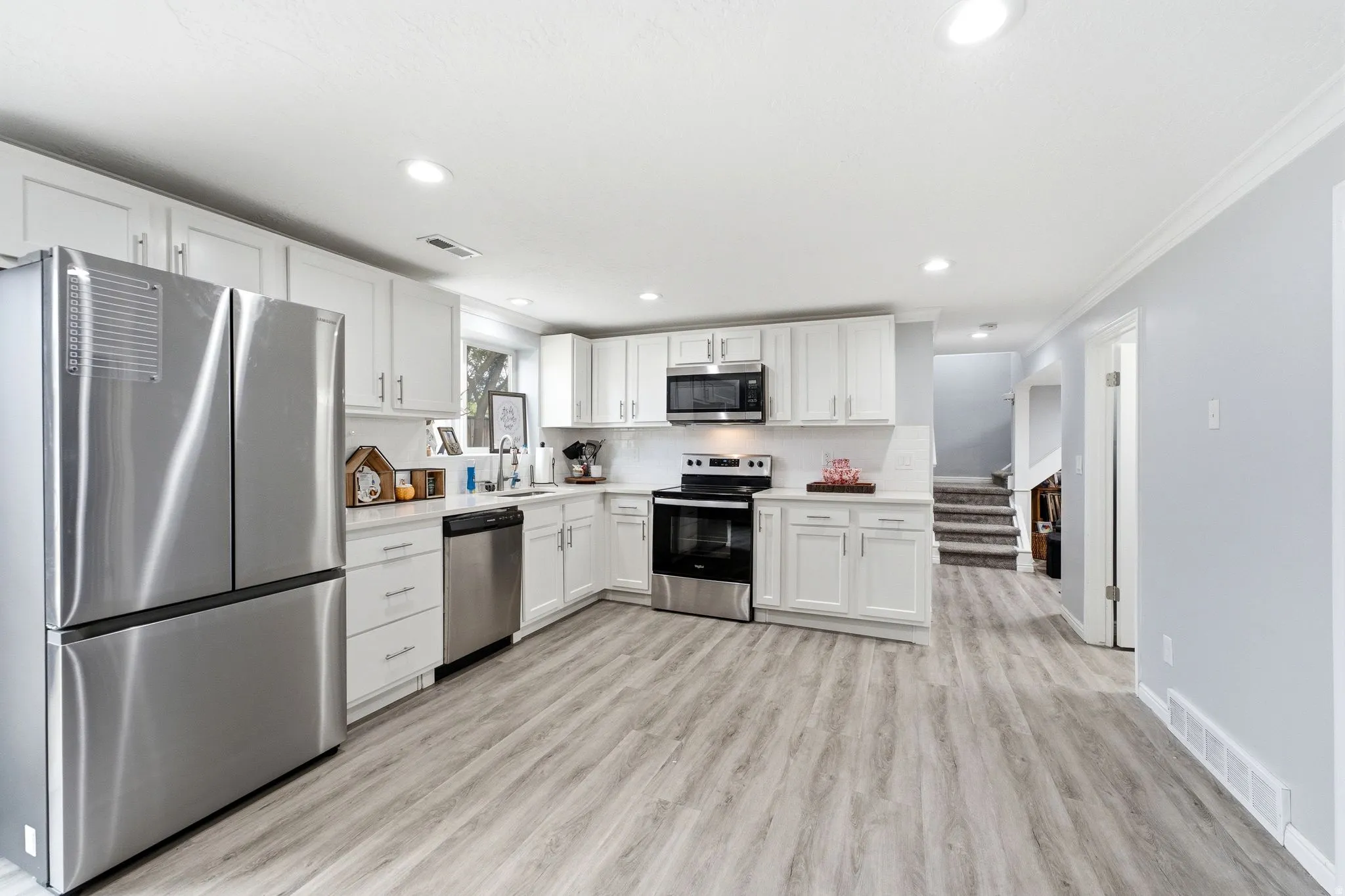 Kitchen featuring white cabinetry, stainless steel appliances, light-toned wood-finish flooring, and recessed lighting