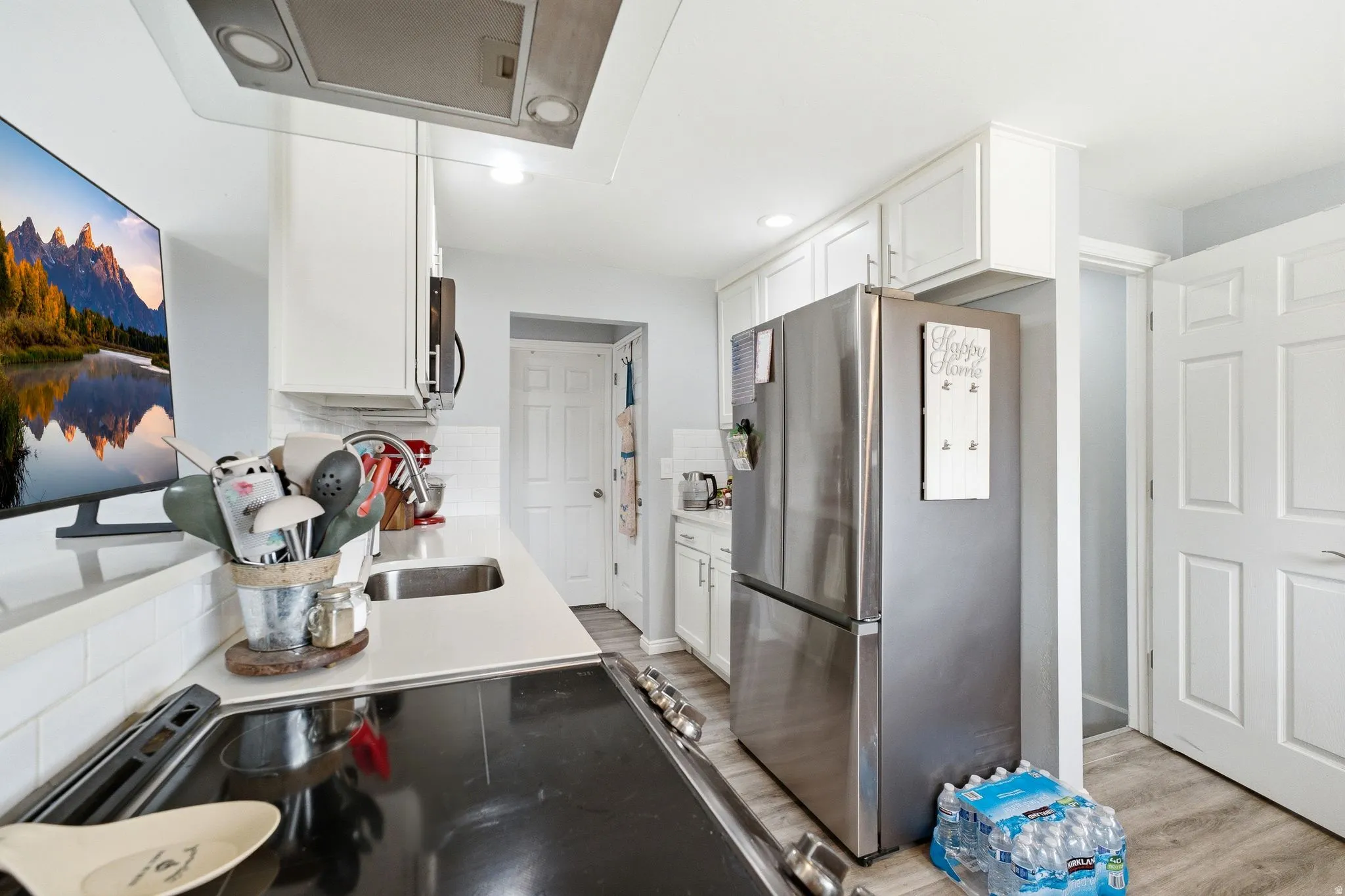 White shaker cabinetry, stainless steel appliances, white subway tile backsplash, white countertops, and wood-finish flooring