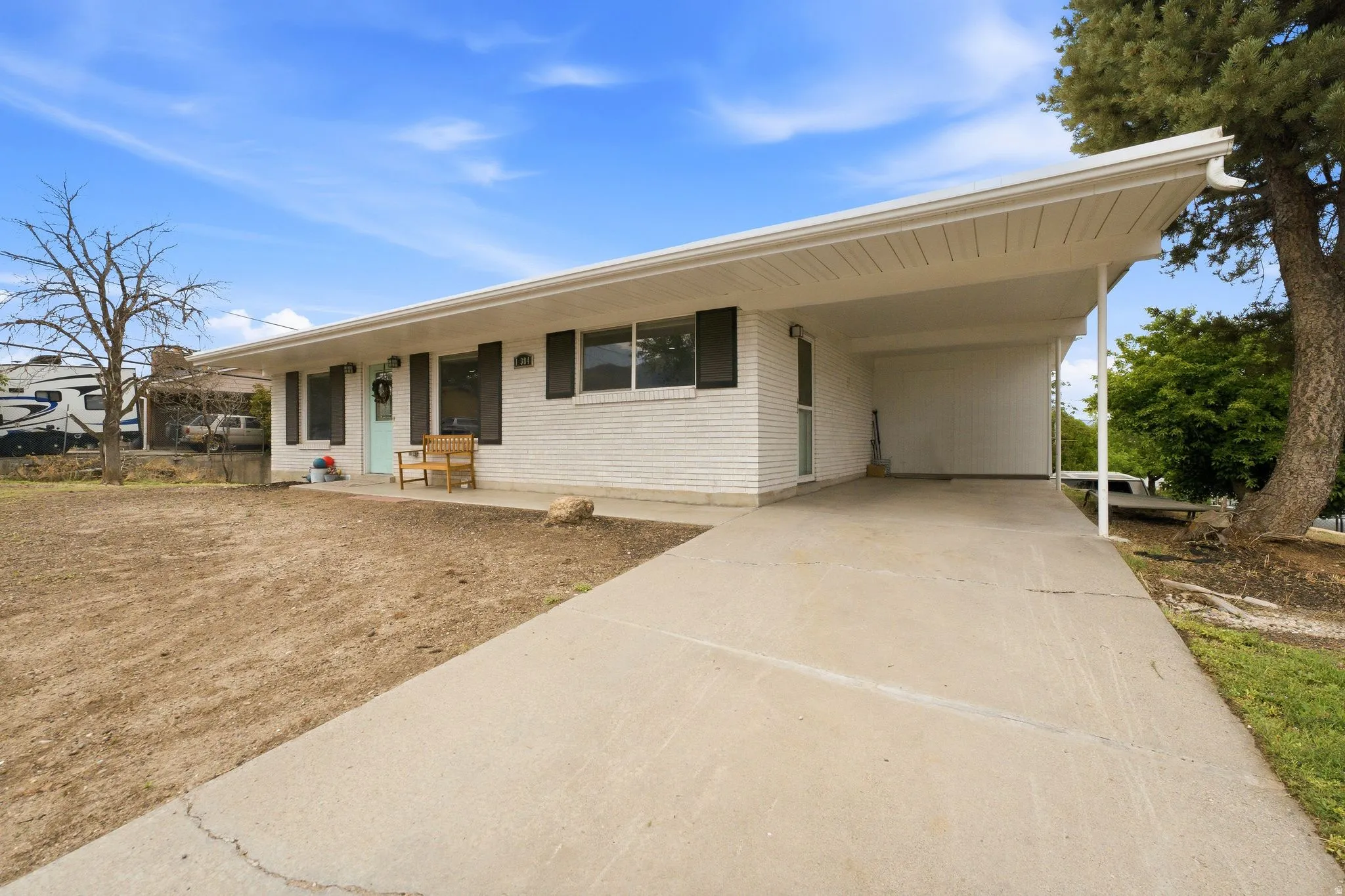 White brick exterior, black window shutters, light blue front door, covered carport, concrete driveway