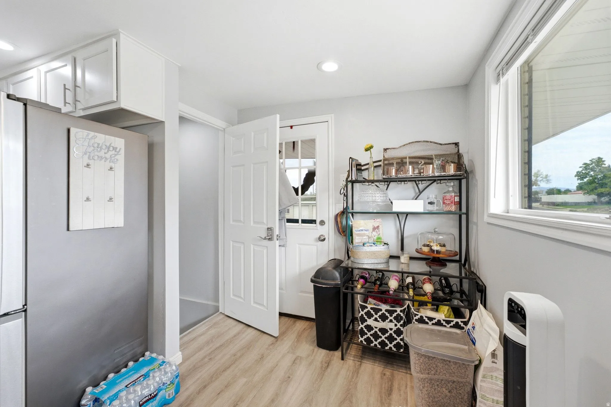 Light wood-finish flooring, white paneled door, recessed lighting, white window trim, and white upper cabinetry