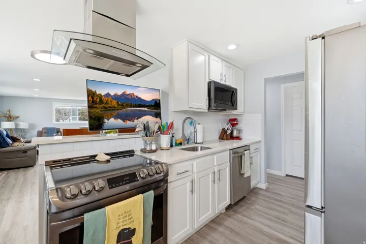 Kitchen featuring white cabinetry, stainless steel appliances, quartz countertops, white subway tile backsplash, and wood-finish flooring