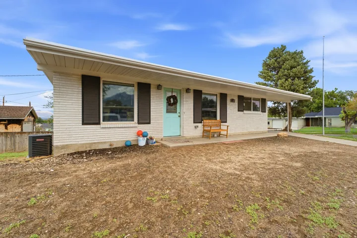White brick exterior with dark shutters, covered concrete porch, and light blue entry door