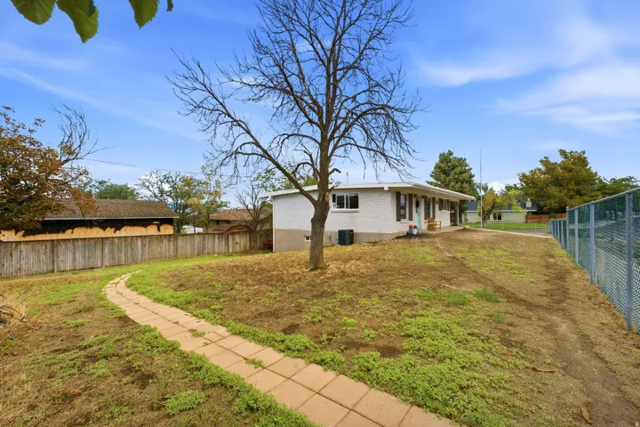 Expansive outdoor space featuring a paved walkway, mature tree, and chain-link fencing