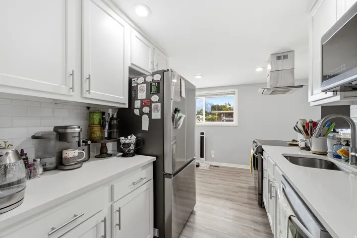 White shaker cabinetry, stainless steel appliances, subway tile backsplash, white countertops, and wood-finish flooring