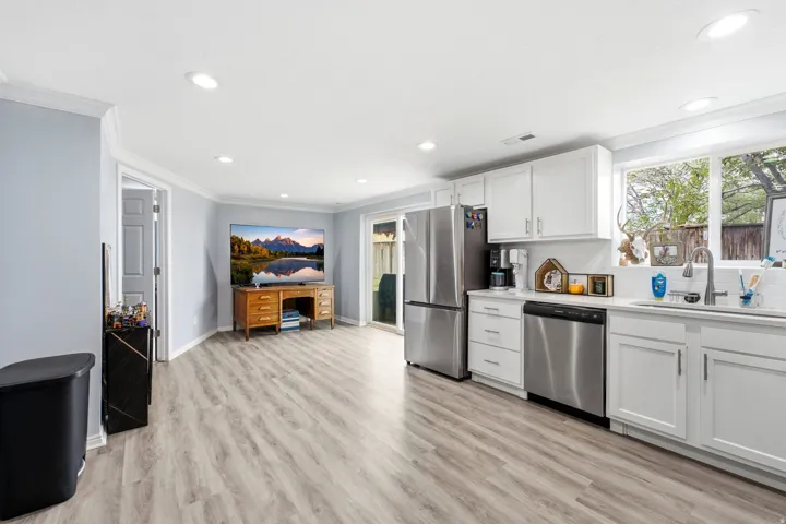 Open-concept living space with wood-finish flooring, recessed lighting, white cabinetry, stainless steel appliances, and a full-size window