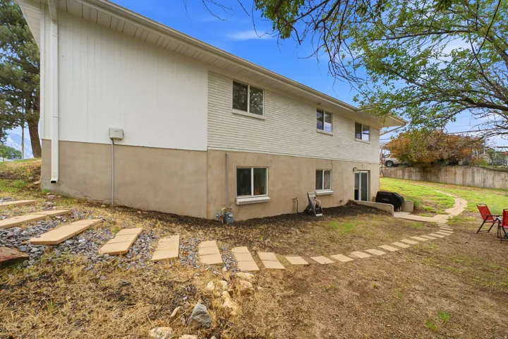 Expansive yard with a sloped landscape, featuring a paved pathway, mature trees, and a concrete patio with a sliding glass door