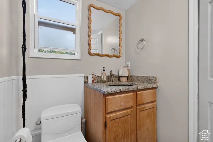 Single-pane window, white wainscoting, light wood-finish vanity, stone-finish countertop, and a built-in sink with a single-handle faucet
