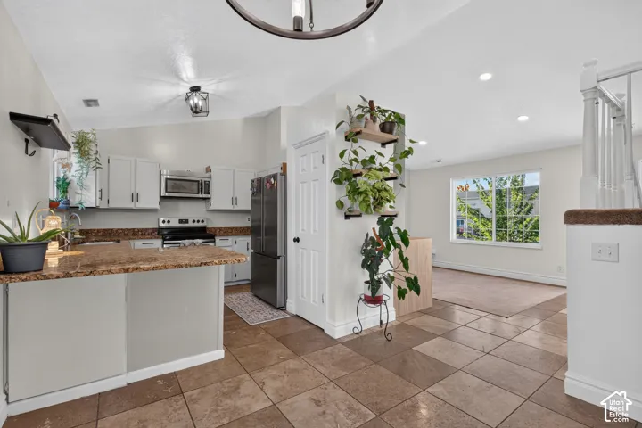 Kitchen with granite countertops, stainless steel appliances, white cabinetry, and tile flooring