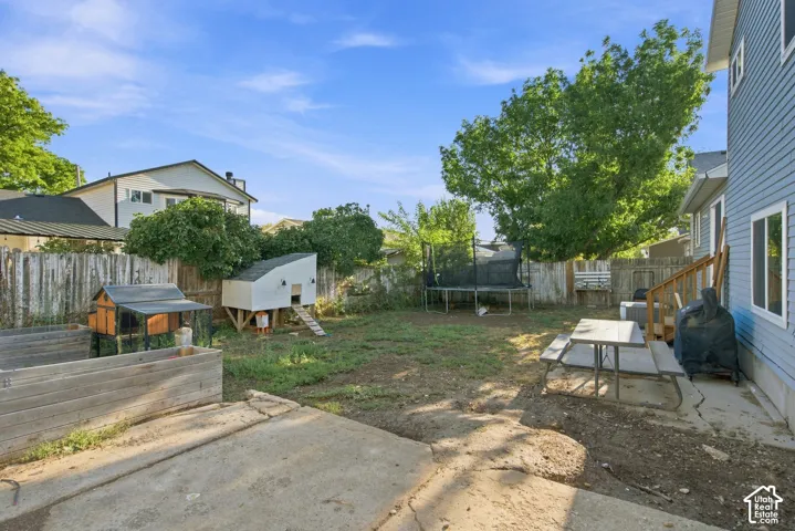 Backyard space featuring a concrete patio, wooden fence, mature trees, and raised garden beds