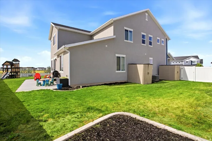 Expansive backyard featuring a concrete patio, a manicured lawn, and two detached storage sheds