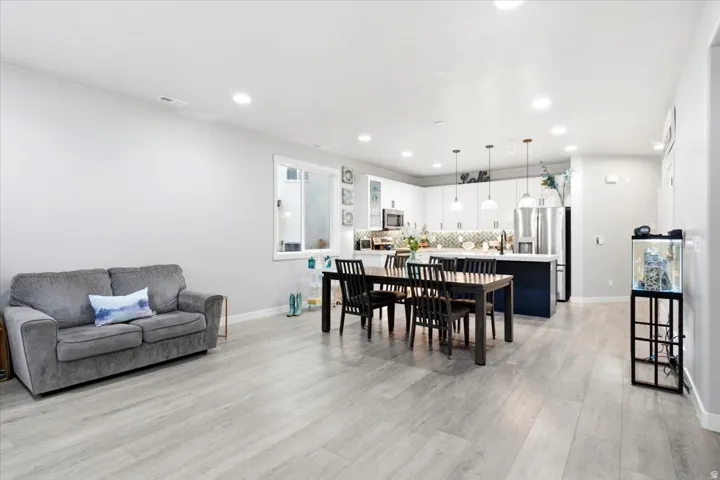 Open-concept living space featuring wood-finish flooring, recessed lighting, a modern kitchen with white cabinetry, a dark-toned island, and stainless steel appliances
