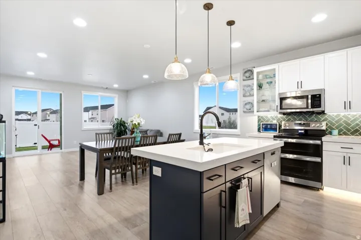 Kitchen featuring an island with a built-in sink, white cabinetry, stainless steel appliances, and a green tile backsplash