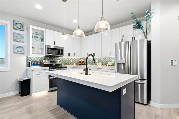 Kitchen featuring a central island with a solid surface countertop, stainless steel appliances, white cabinetry with display glass, a tile backsplash, and overhead pendant lighting