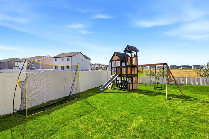 Expansive backyard featuring a lush lawn, white vinyl fencing, and a multi-level playset with swings