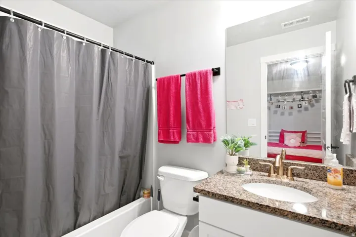 Bathroom featuring a built-in tub with shower, single vanity with a granite-style countertop, integrated sink, and an expansive wall mirror