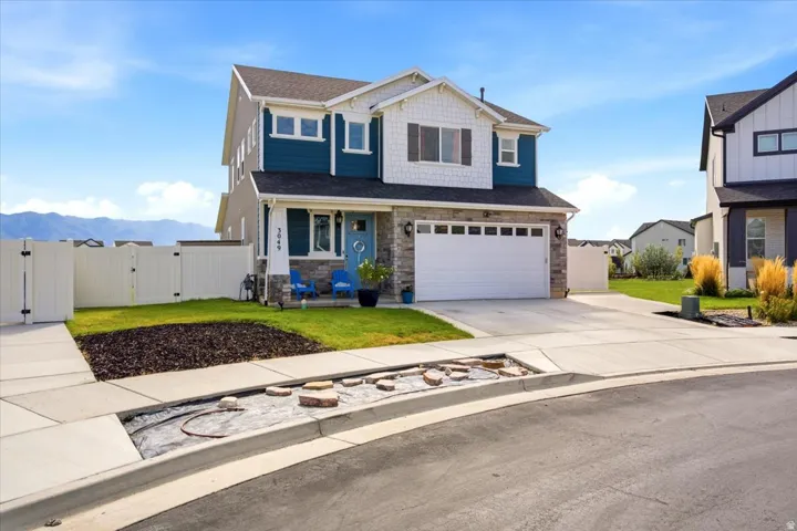 Two-story residence featuring a stone and siding exterior, an attached two-car garage, a concrete driveway, and a fenced side yard