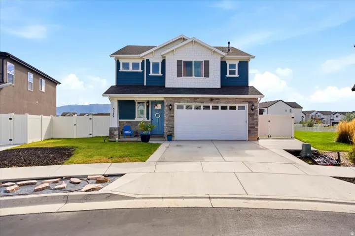Two-story residence featuring blue siding, white shake accents, a stone façade, an attached two-car garage, and a fenced yard