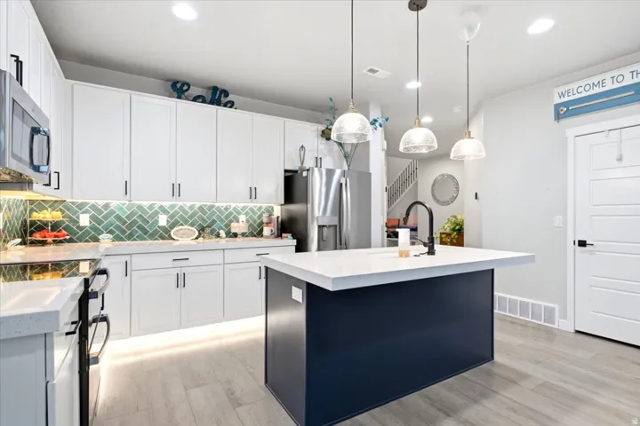 Contemporary kitchen featuring white cabinetry, a large central island with a white countertop, stainless steel appliances, and a green subway tile backsplash