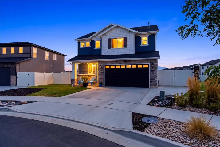Two-story exterior with stone and siding accents, covered porch, attached garage with panel windows, concrete driveway, and landscaped front yard with decorative rock