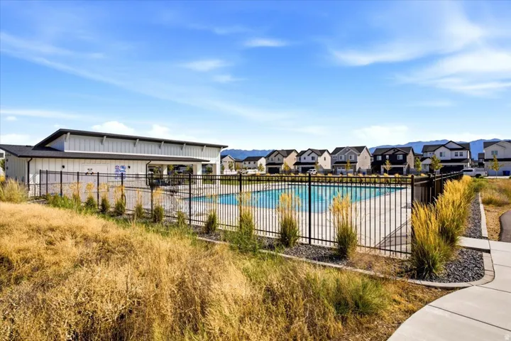 Community pool with surrounding black metal fencing, adjacent clubhouse with covered patio, and concrete pathway