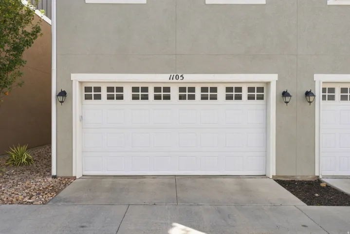 Stucco exterior with white trim, featuring two garage doors with window inserts, and exterior wall sconces