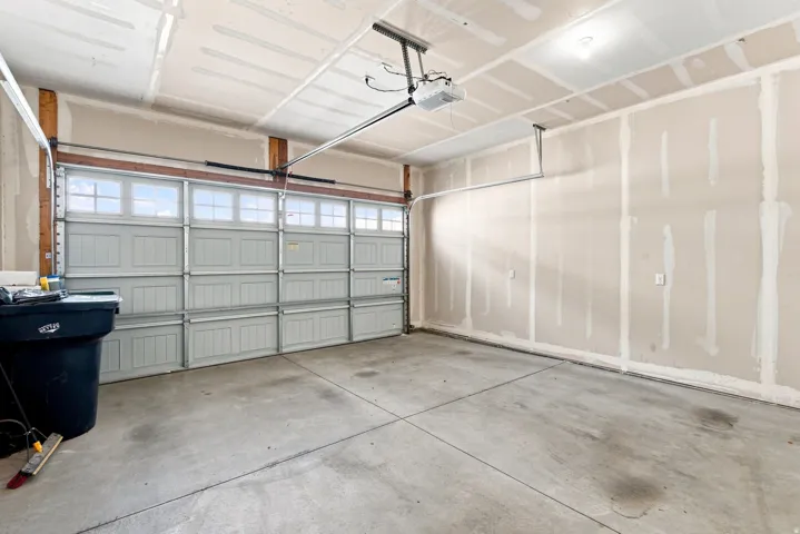 Concrete flooring, unfinished drywall, overhead lighting, and an automatic garage door opener