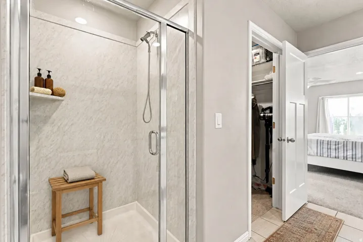 Glass-enclosed shower with a wall-mounted showerhead, built-in shelving, and light-toned wall panels