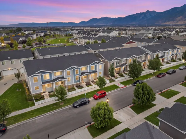 Townhome streetscape featuring varied exterior finishes, landscaped front yards with white fencing, and an expansive mountain range backdrop
