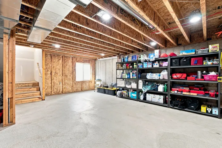 Unfinished basement featuring exposed wood joists, concrete flooring, and an egress window