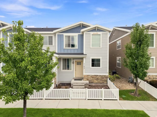 Contemporary facade featuring light blue siding, stone accents, and a white picket fence