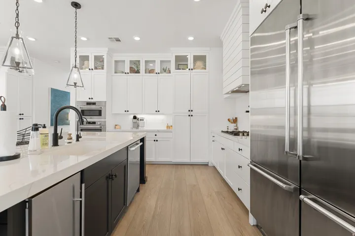 White shaker cabinetry with black hardware, stainless steel appliances, wood-finish flooring, island with integrated dishwasher, and pendant lighting