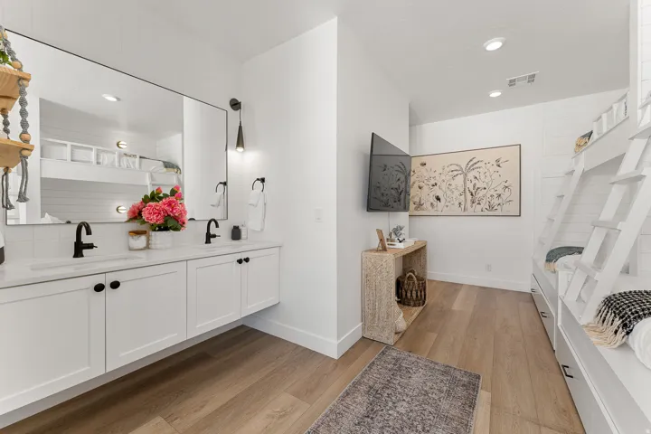 Dual floating vanity with undermount sinks and matte black fixtures, full-width mirror, wood-finish flooring, recessed lighting, and built-in bunk beds with storage drawers