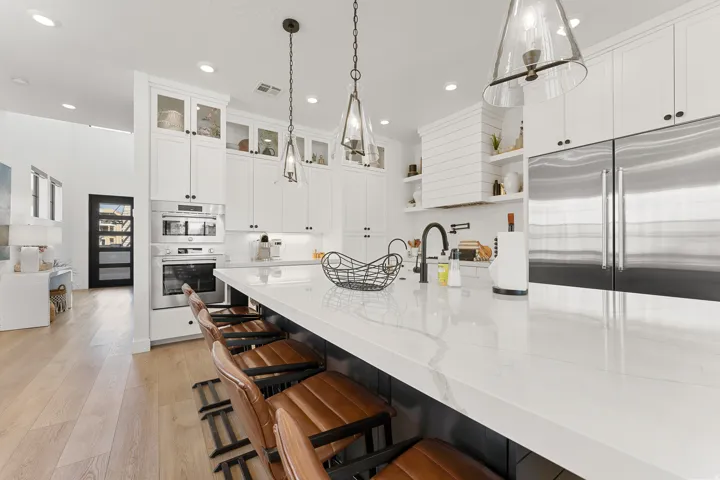 Kitchen featuring a white countertop island, stainless steel appliances, white cabinetry, wood-finish flooring, and pendant lighting