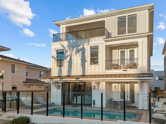 Three-story property featuring a ground-level pool, glass panel fencing, and two upper-level balconies with black railings