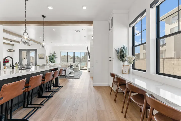 Open-concept living space featuring wood-finish flooring, a kitchen island with stone countertop, exposed wood beams, and a built-in window counter