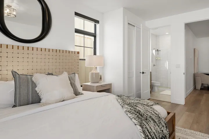 Wood-finish flooring, woven headboard, dual sliding closet doors, and an en-suite bathroom with subway tile shower
